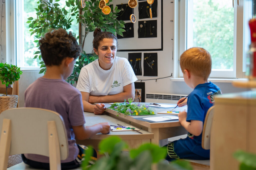 Barn som målar av stilleben av plockade vildvuxna blommor tillsammans med sin förskolepedagog